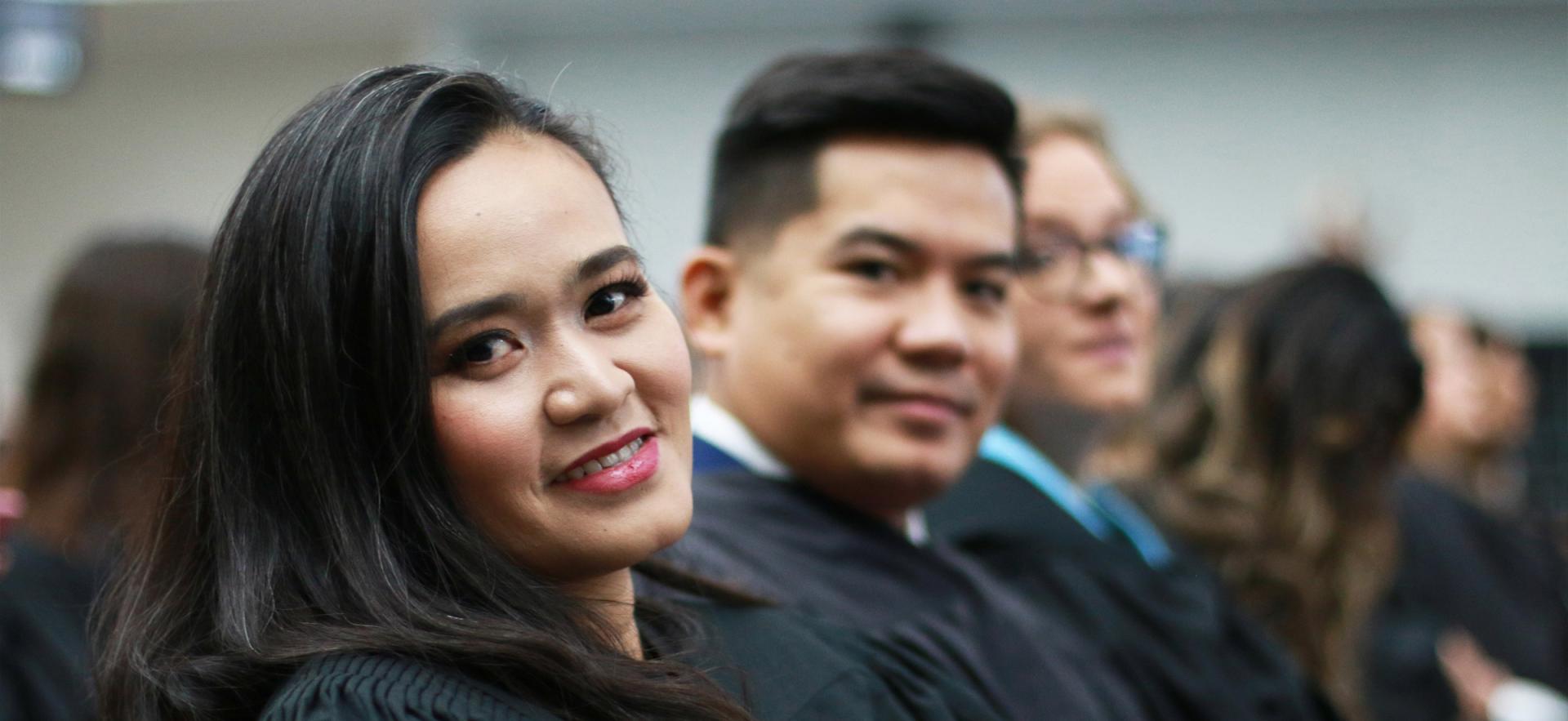 Student in graduation robe sitting at convocation and looking at camera with other students around