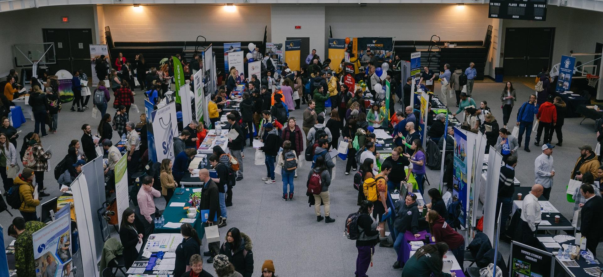 Annual Career Fair photo of employer booths and job seekers in the gym