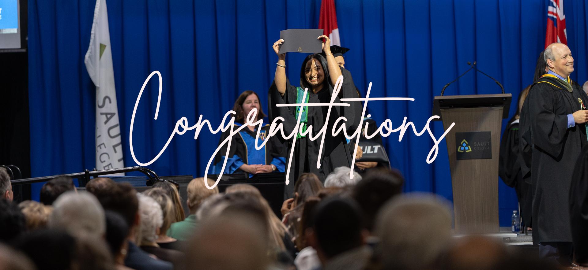 Graduate on the stage raising diploma above her head at convocation