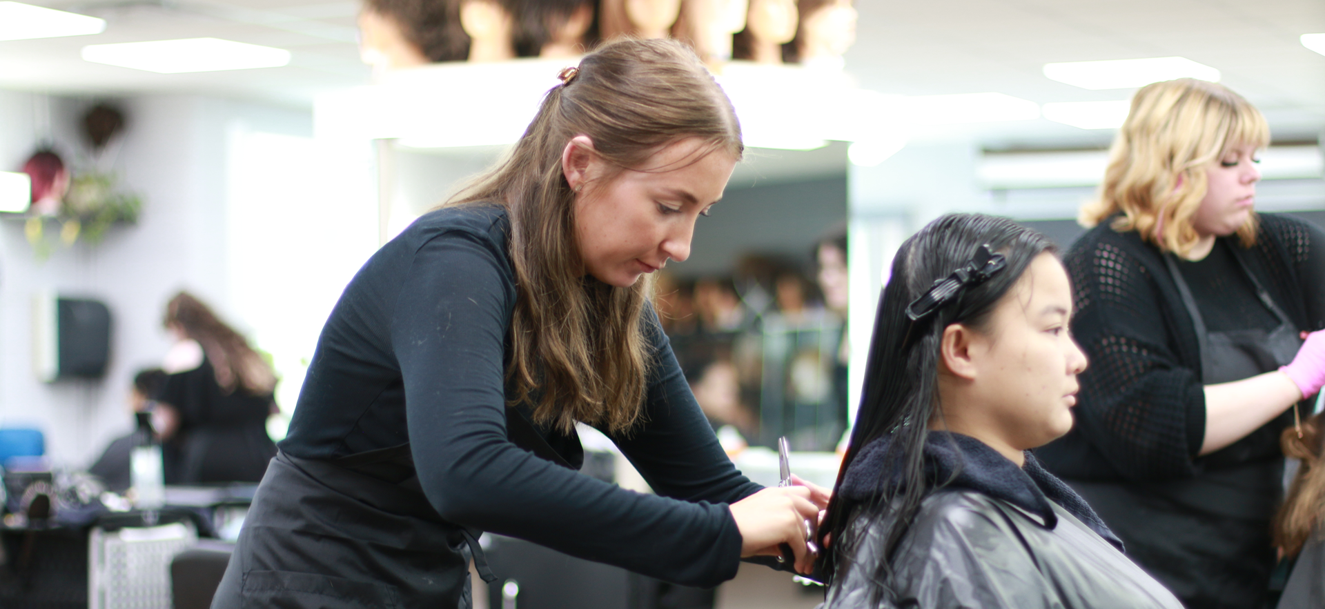 Hairstyling student cutting client's hair in salon