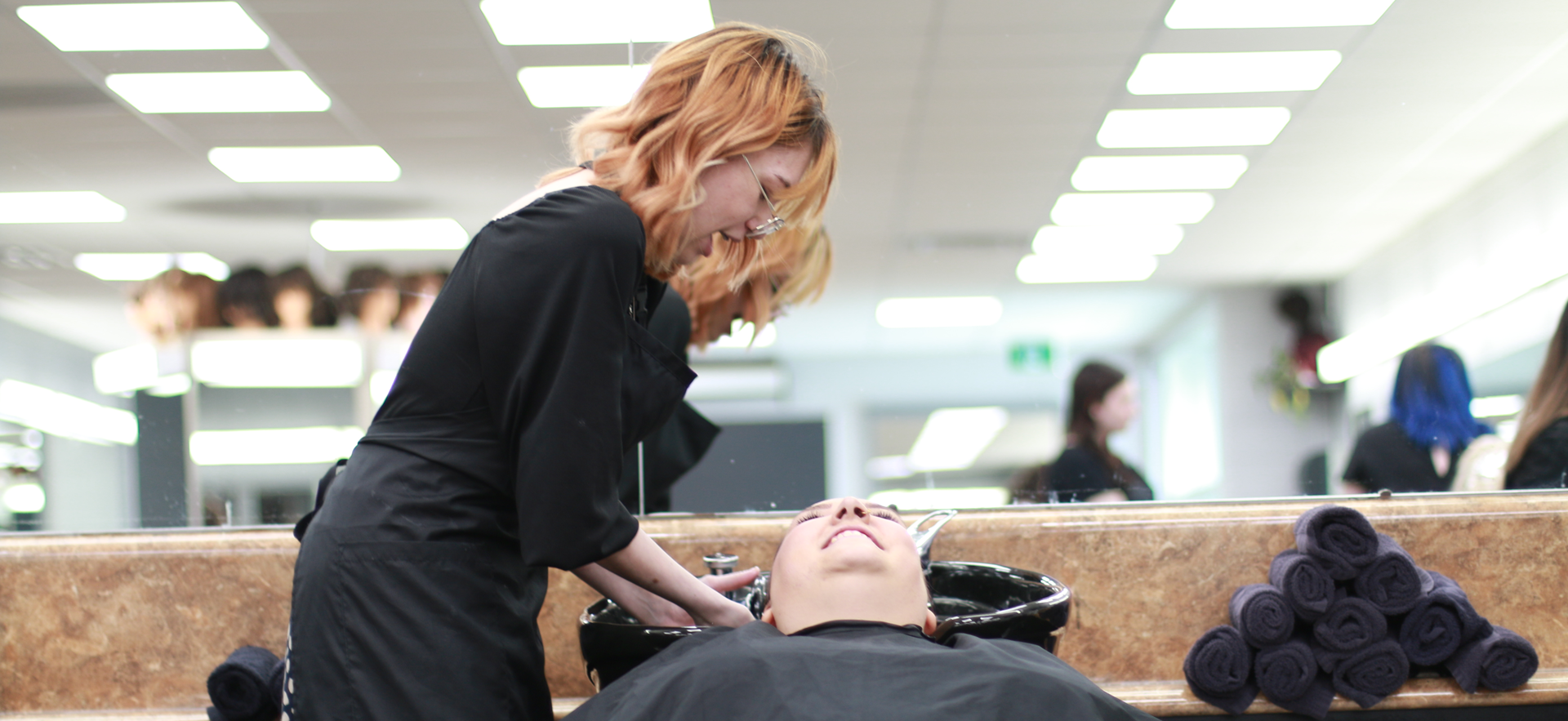 Hairstyling student washing client's hair in salon
