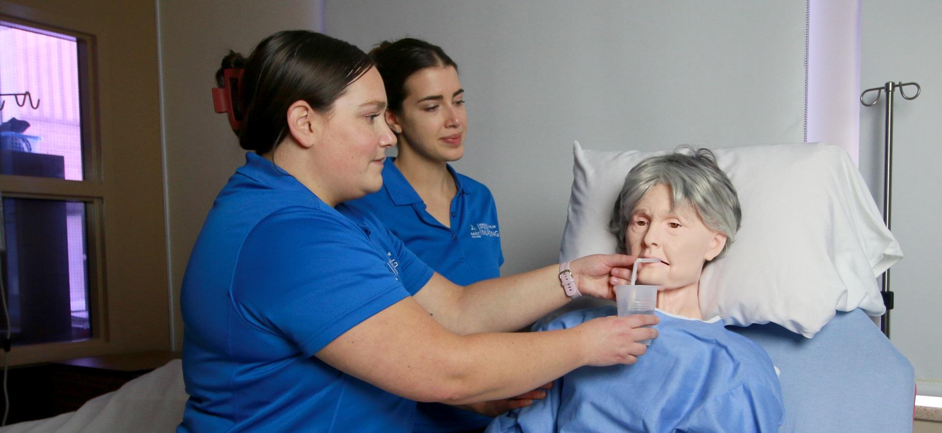 Nursing students assisting sim manikin with drinking water through a straw