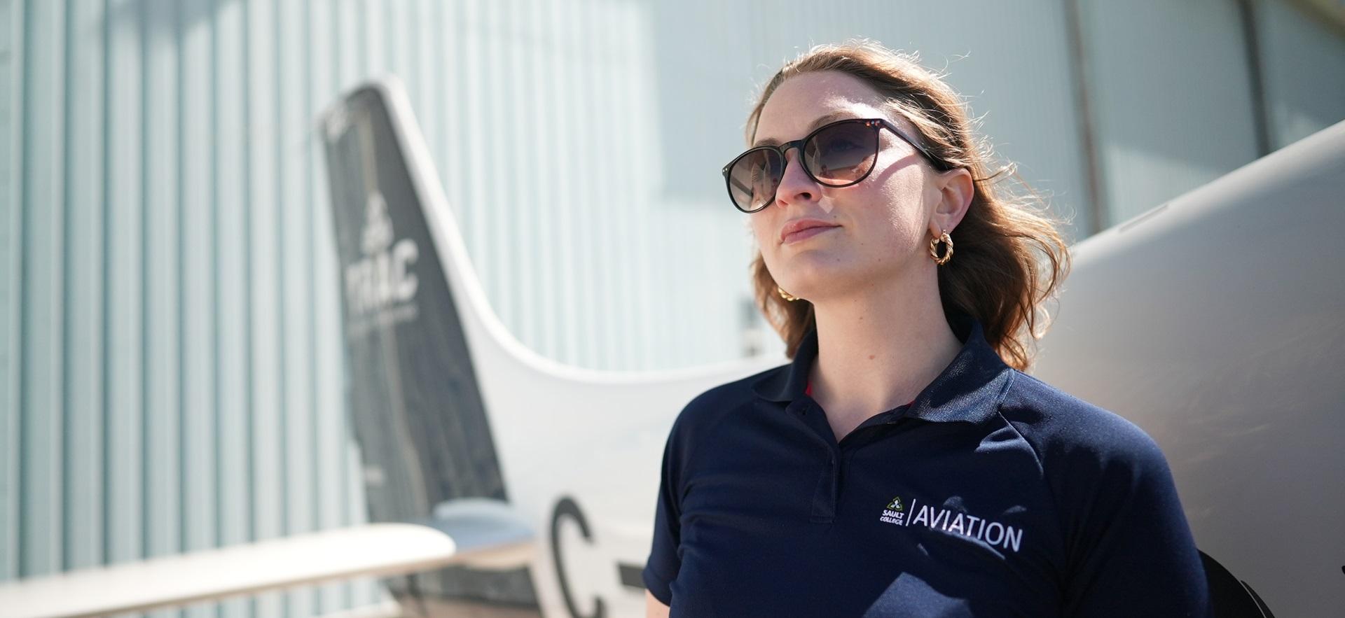 Aviation student Amanda looking up at the sky standing in front of a plane