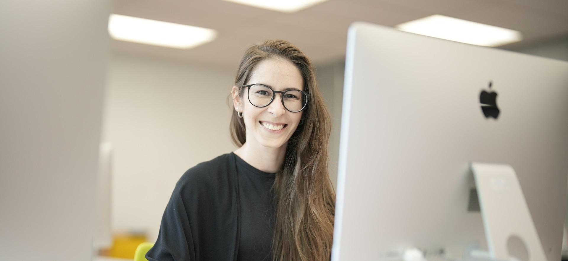 Graphic Design student smiling at camera working on mac in design lab