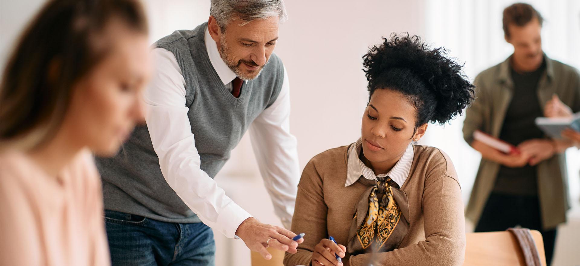 Adults dressed professionally in a room standing or sitting reviewing materials