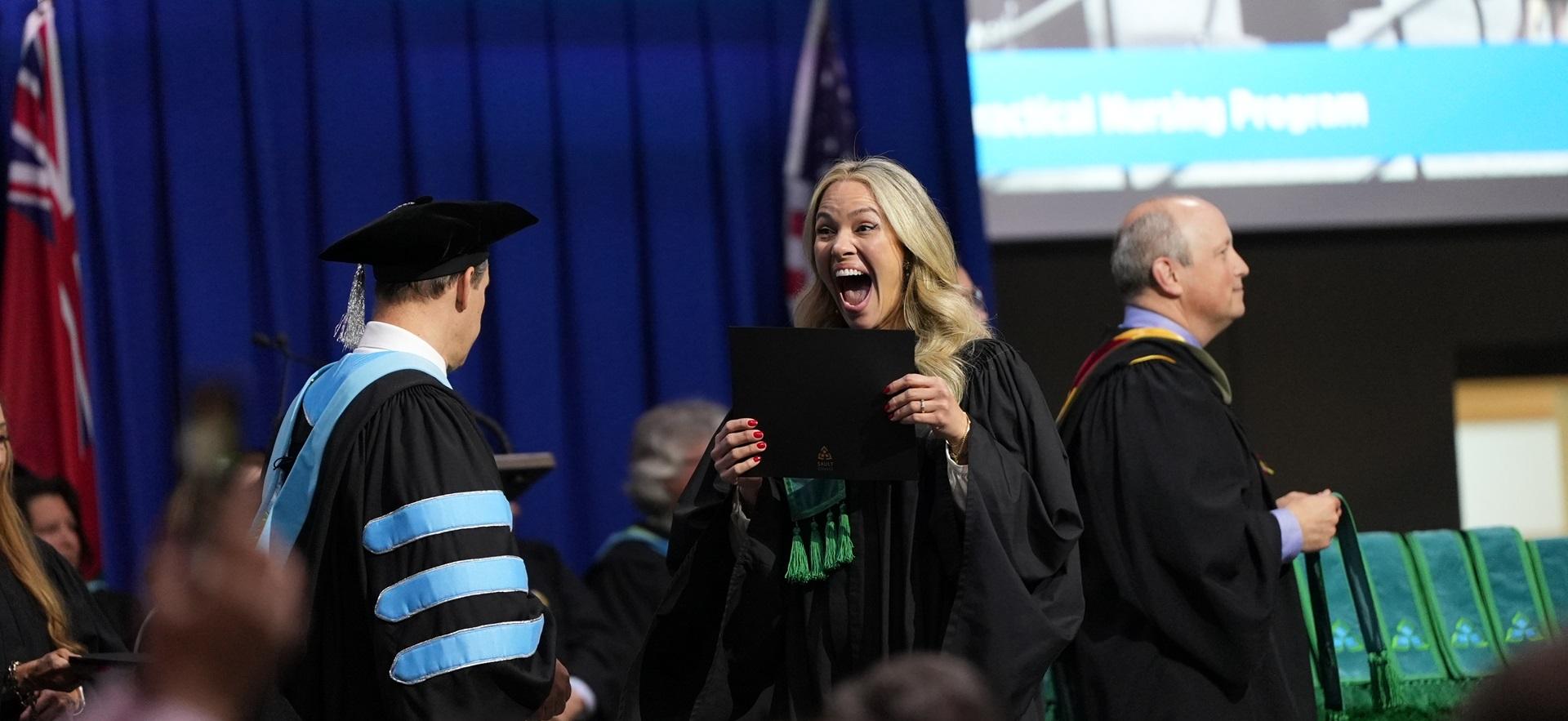 Excited graduate holding diploma as she walks across stage at convocation