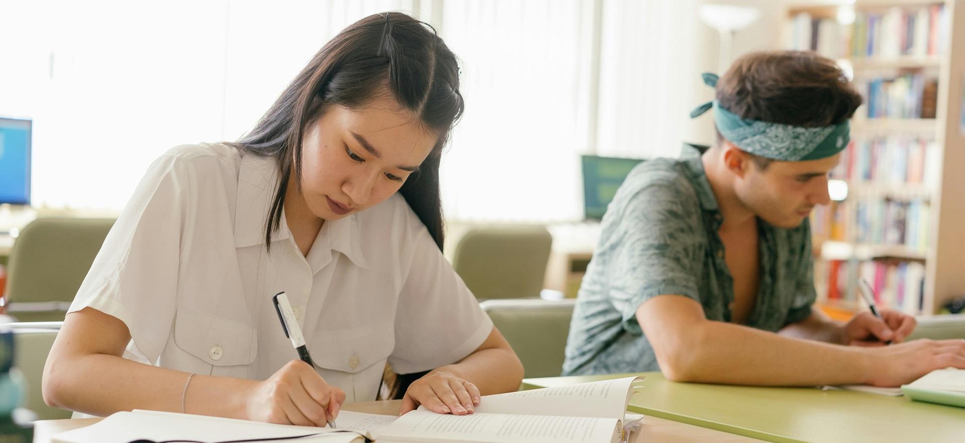 Two students seated next to each other at a table and writing