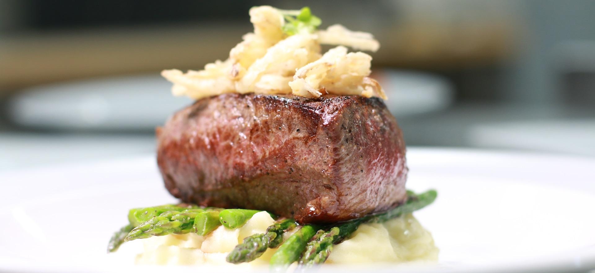 Culinary plated meal with steak on bed of mashed potato and asparagus