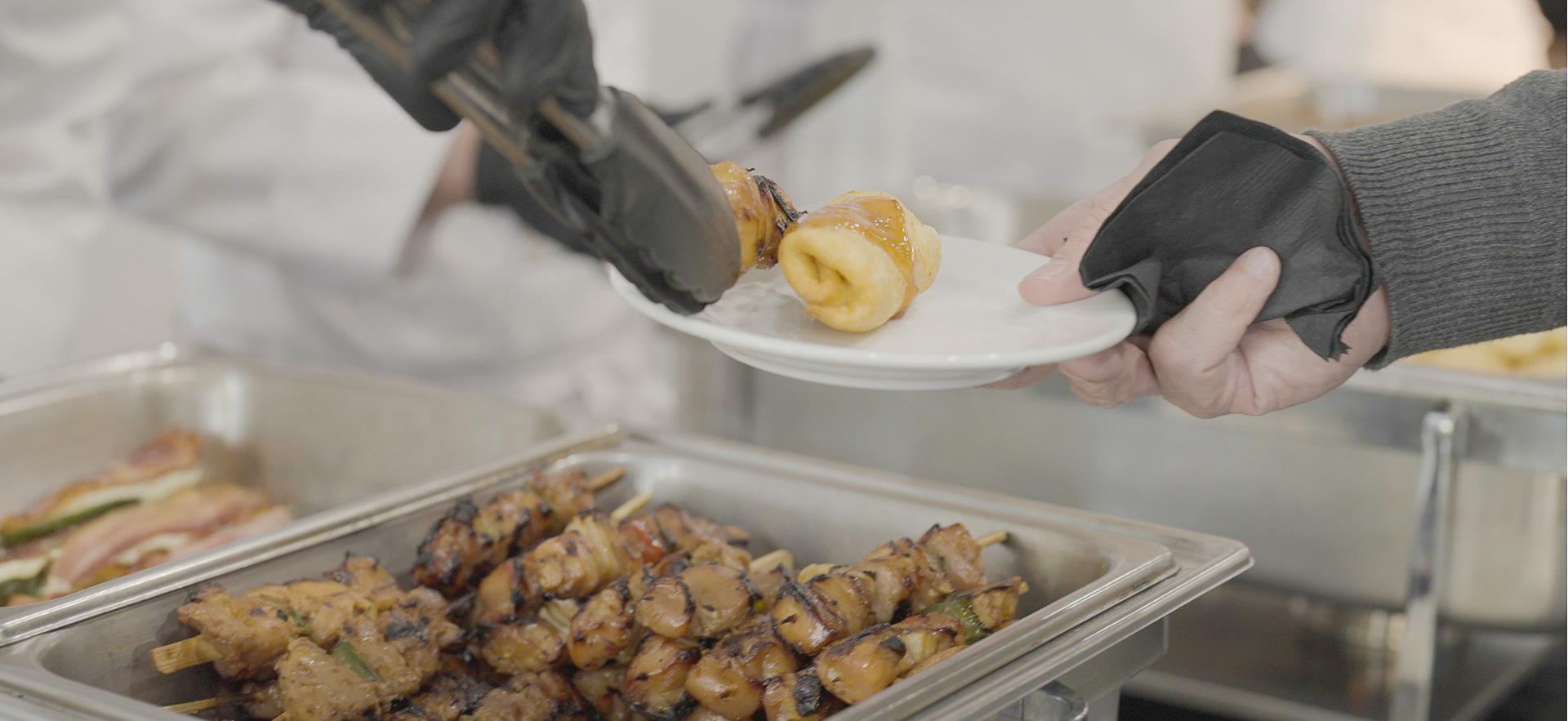 Culinary student serving meat skewer on a guest's plate at event