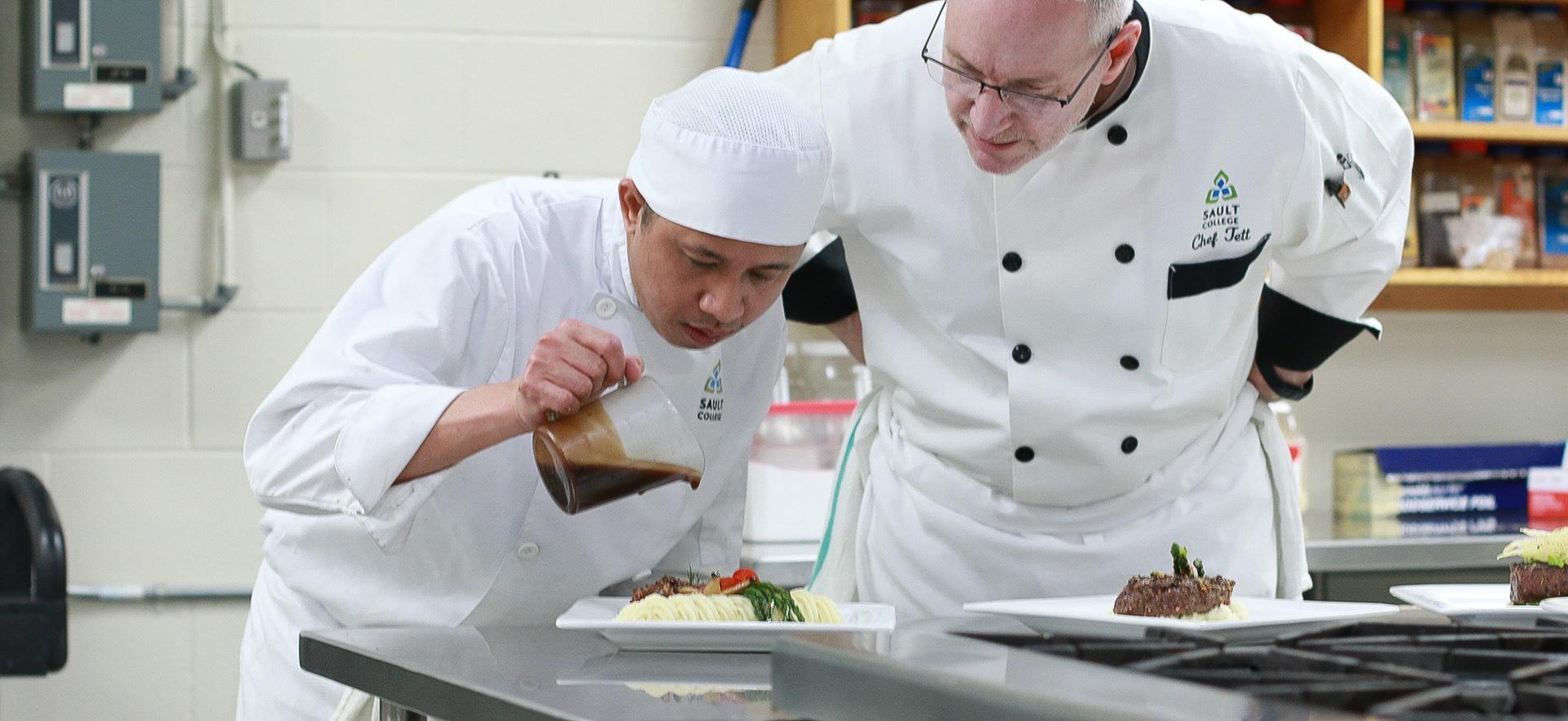 Culinary student show with instructor pouring glaze on a plated dish