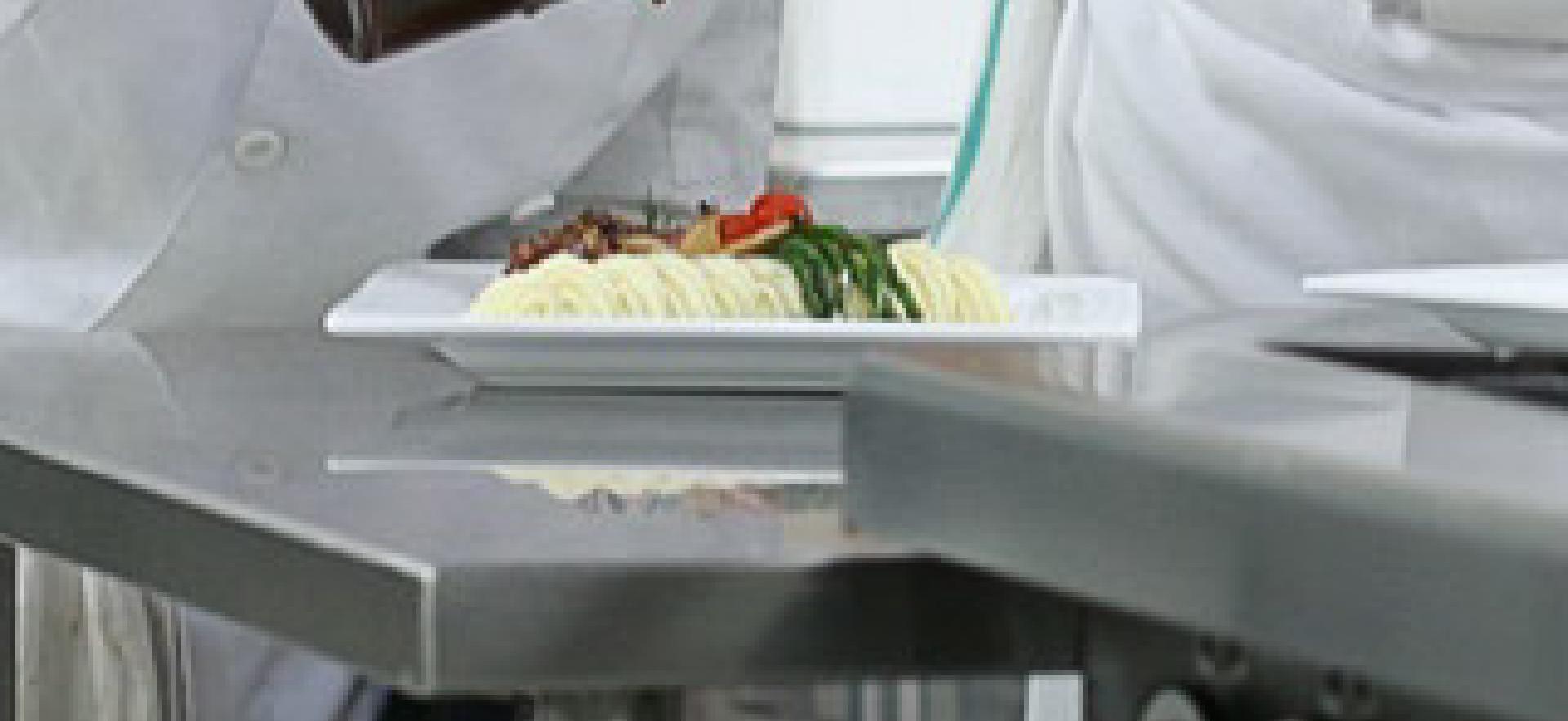 Culinary student with instructor shown about to pour glaze on plated meal