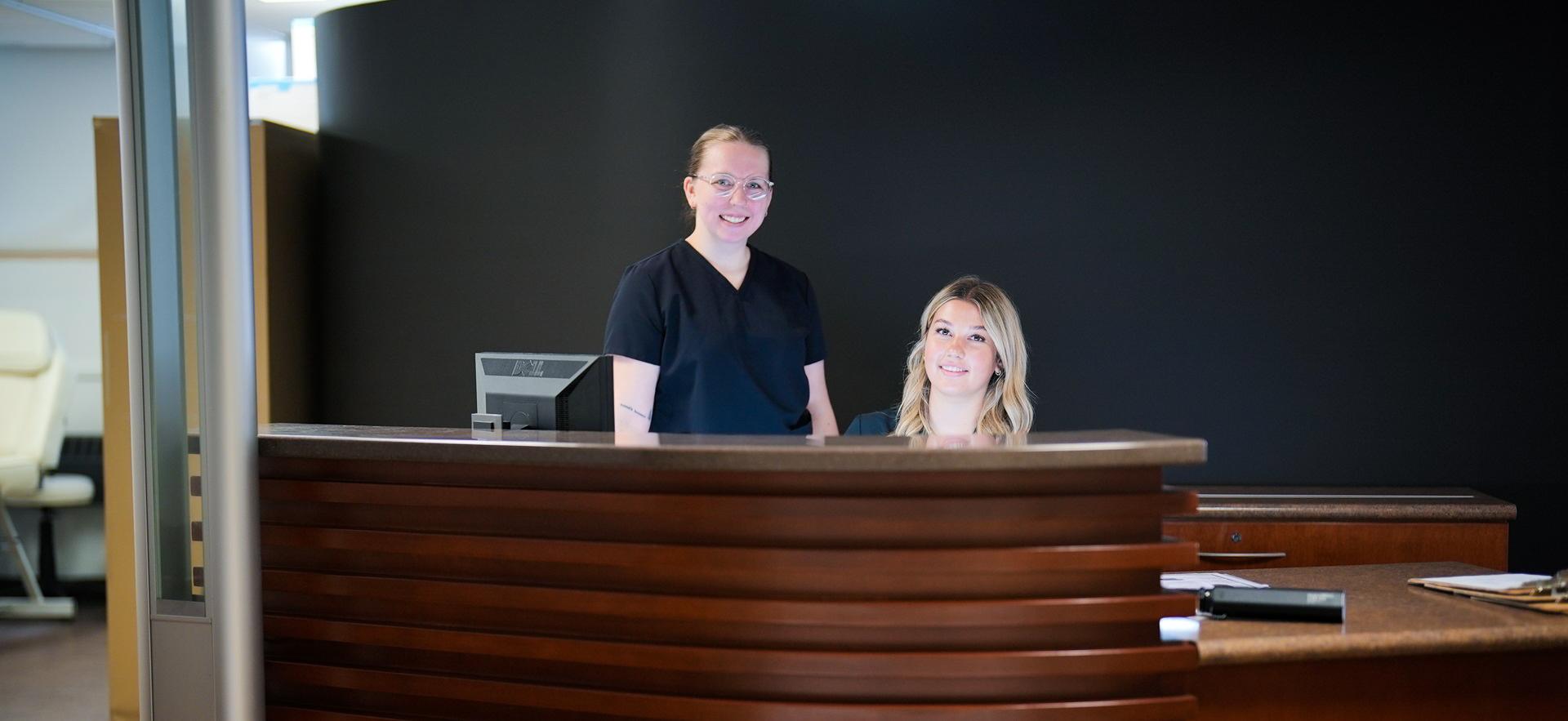 Esthetician students smiling behind reception desk in the Spa