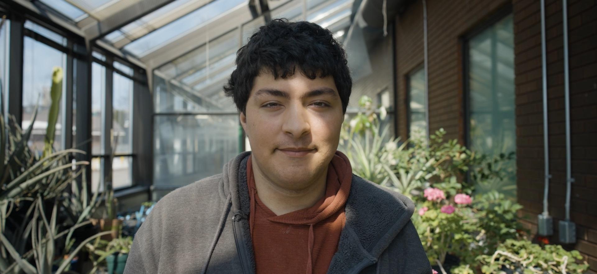 CICE student looking straight at camera with SONE greenhouse in background