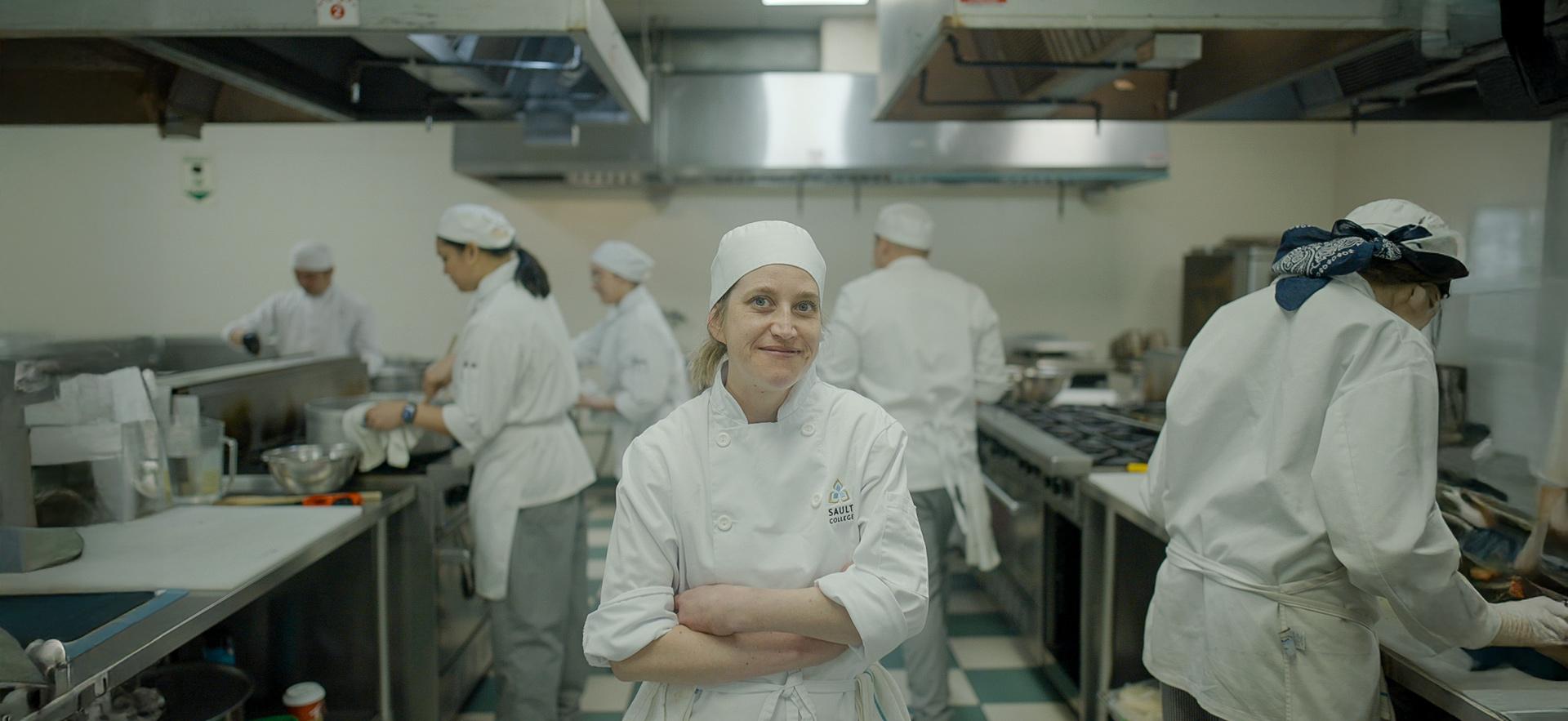 CICE student posed in the kitchen with Culinary students at work