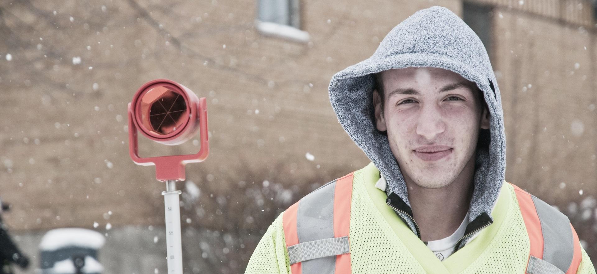 Civil Engineering student with hood on outside with snow falling doing checks
