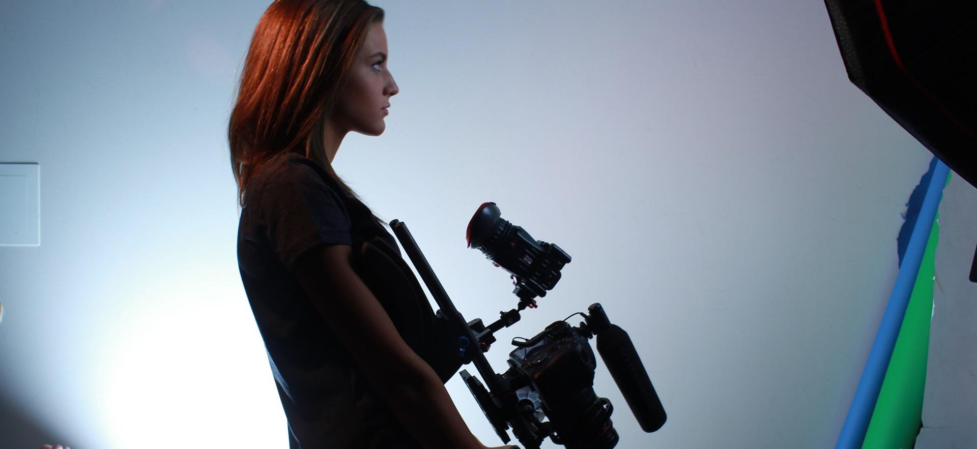 Film student standing and looking to side holding film equipment