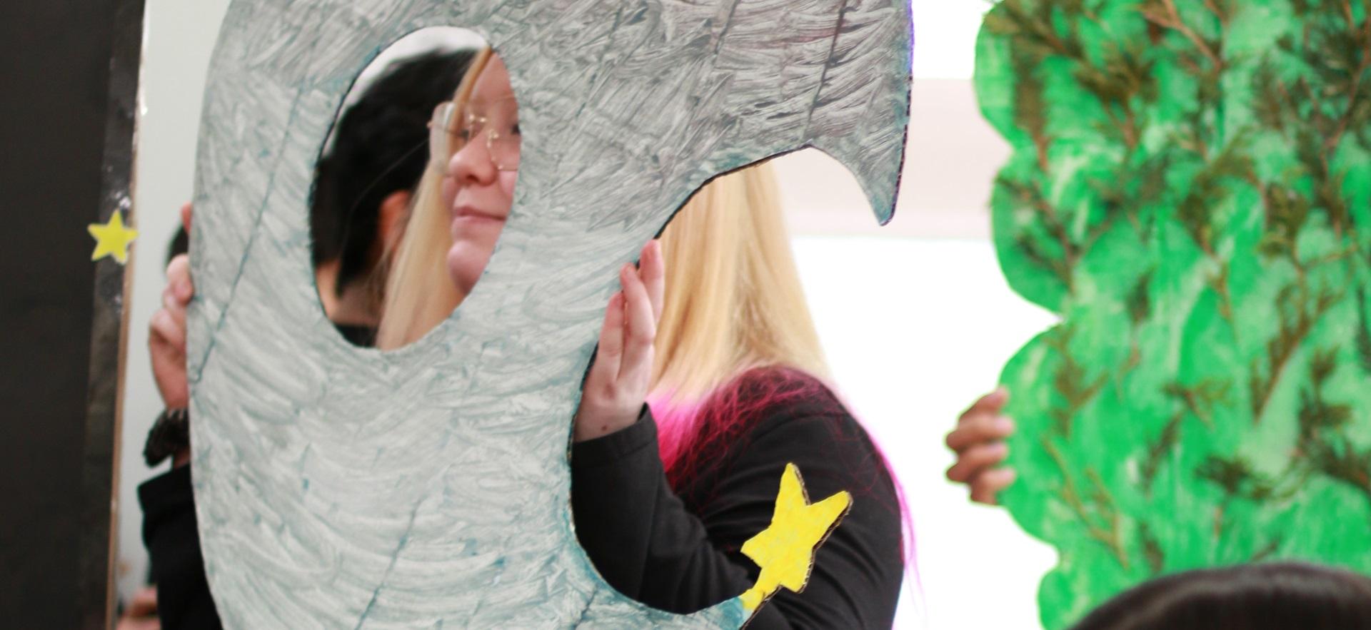 ECE student holding a large paper moon with face cut out for storytelling