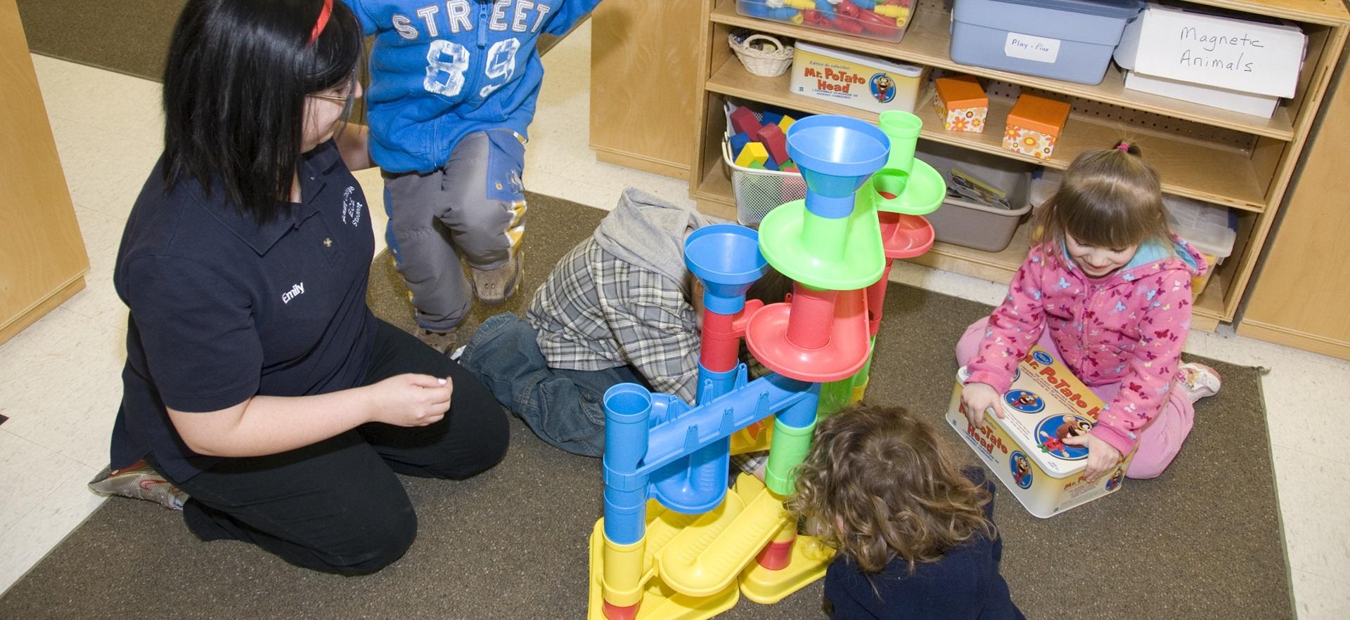 ECE student sitting on floor with children playing with a toy