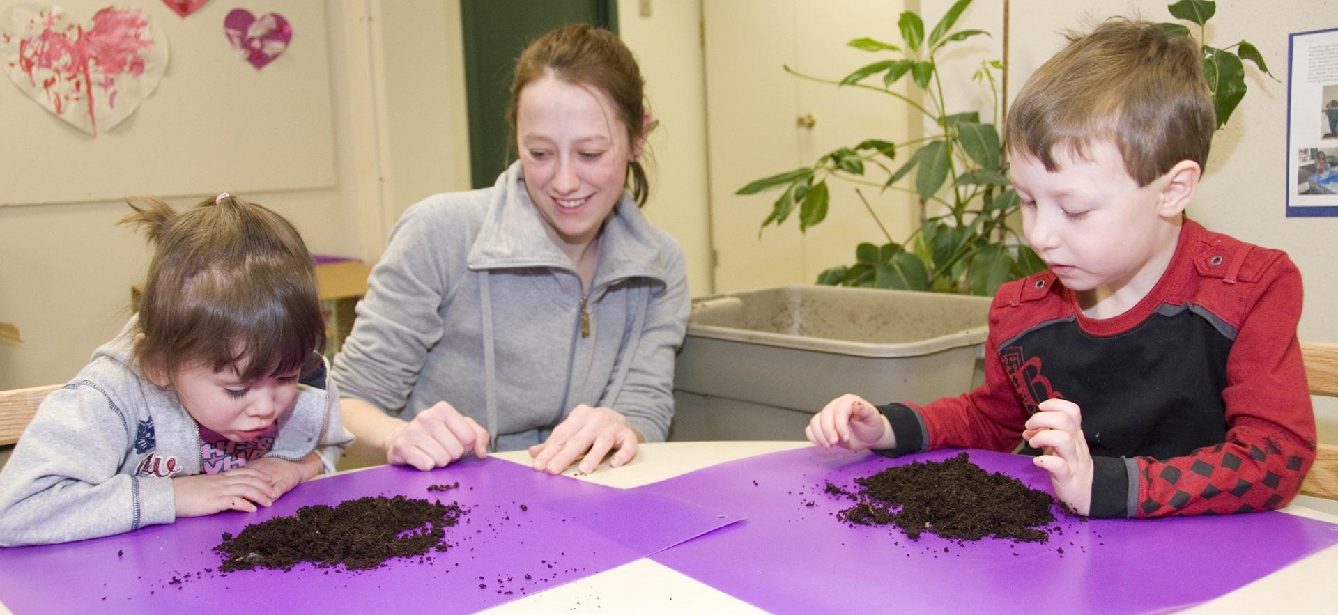 ECE sitting at table with two children with placemats and potting soil
