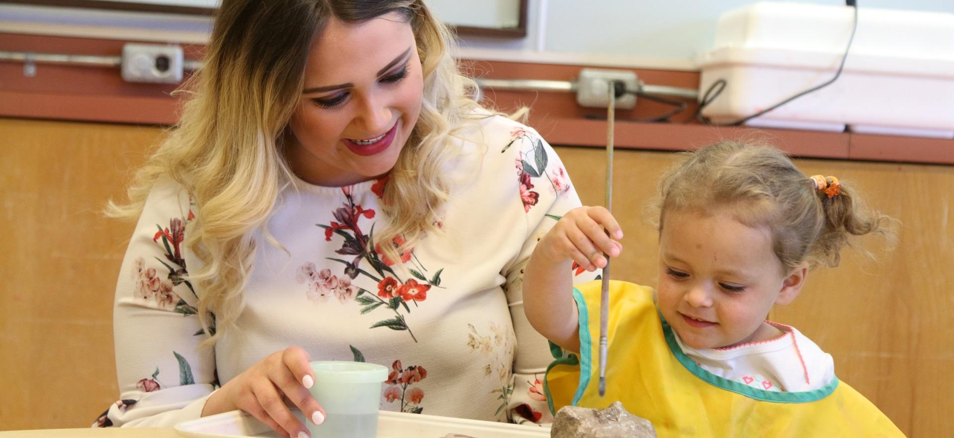 ECE sitting at table with child painting a rock