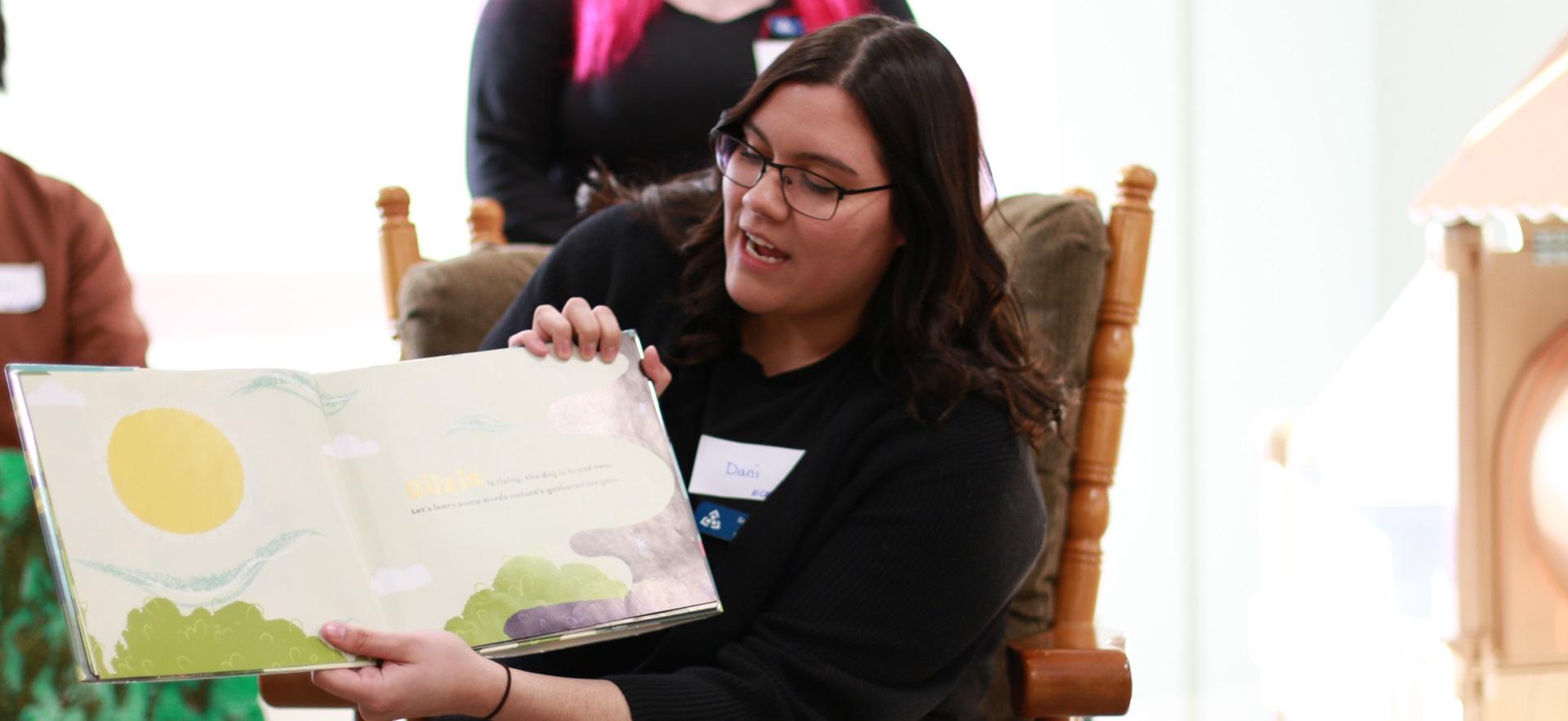 ECE student sitting in chair reading book to children