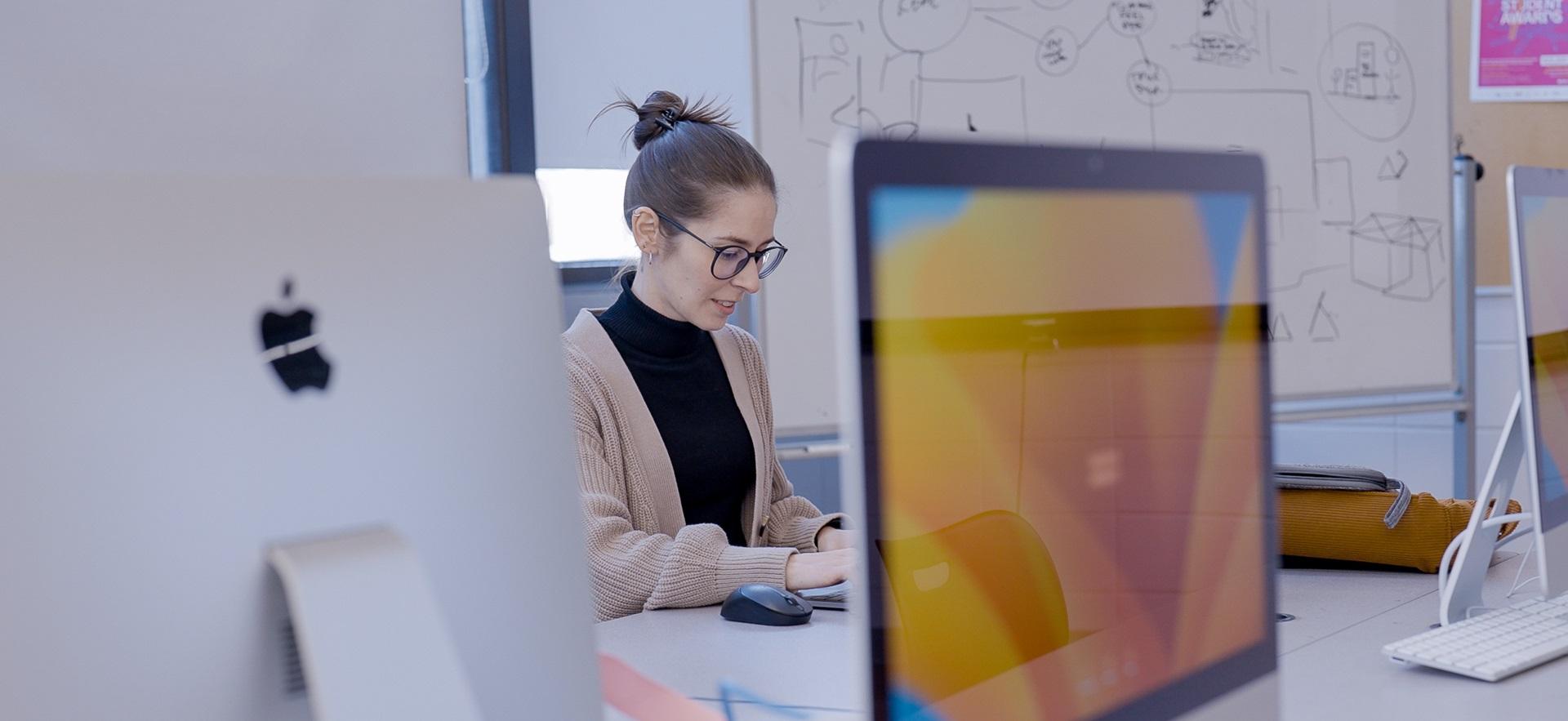 Graphic design student working in the Mac lab with computers visible