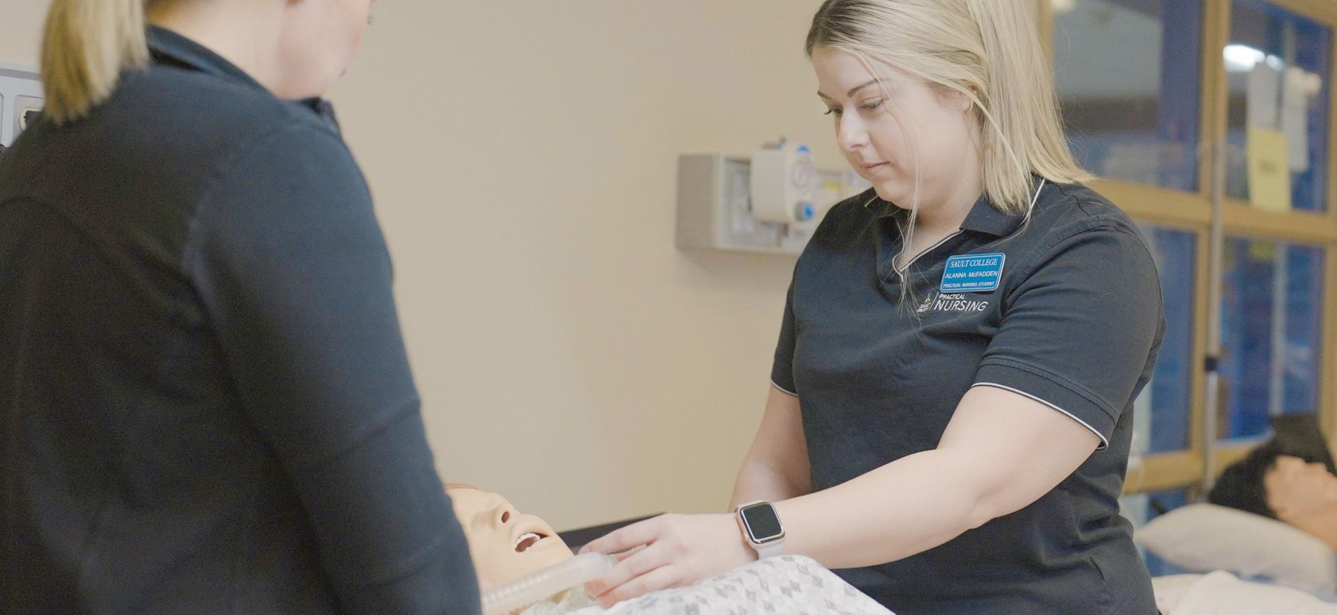 Nursing student working with classmate on a simulation manikin