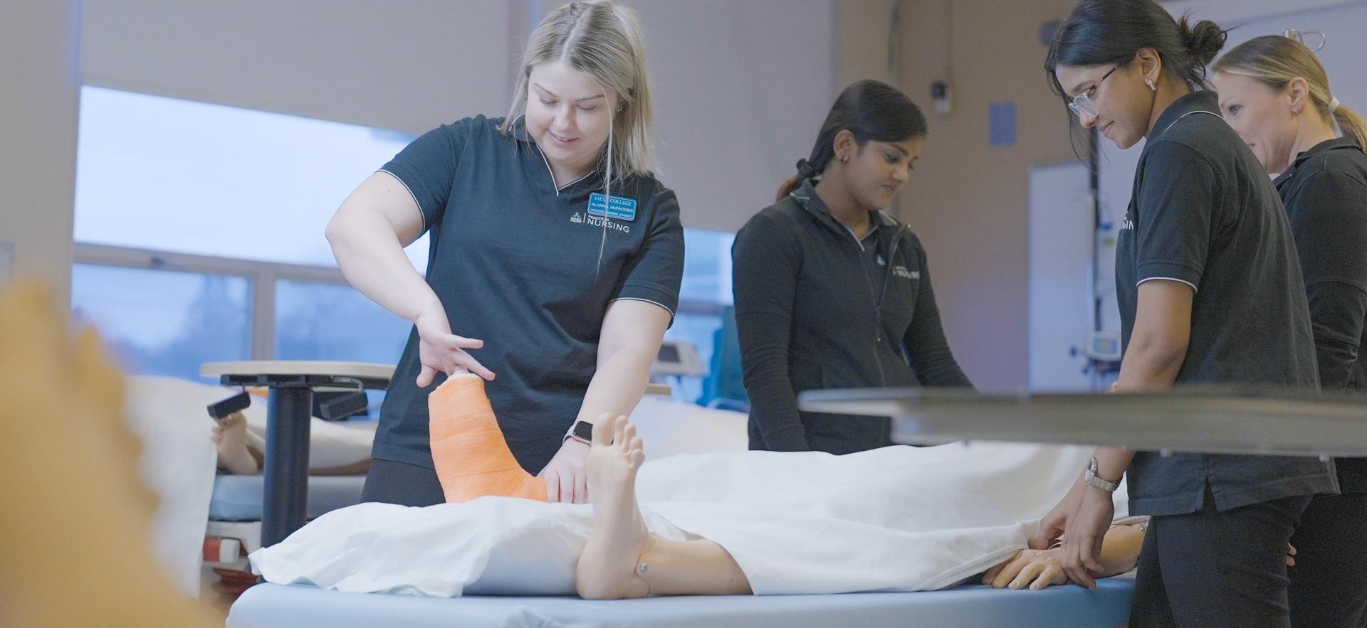 Nursing students gathered around sim on a bed and looking at casted foot