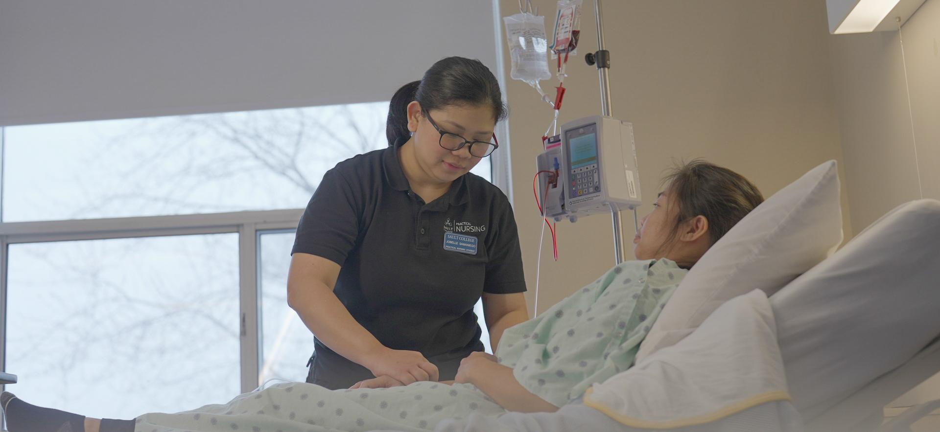 Nursing student checking IV of classmate posing as patient