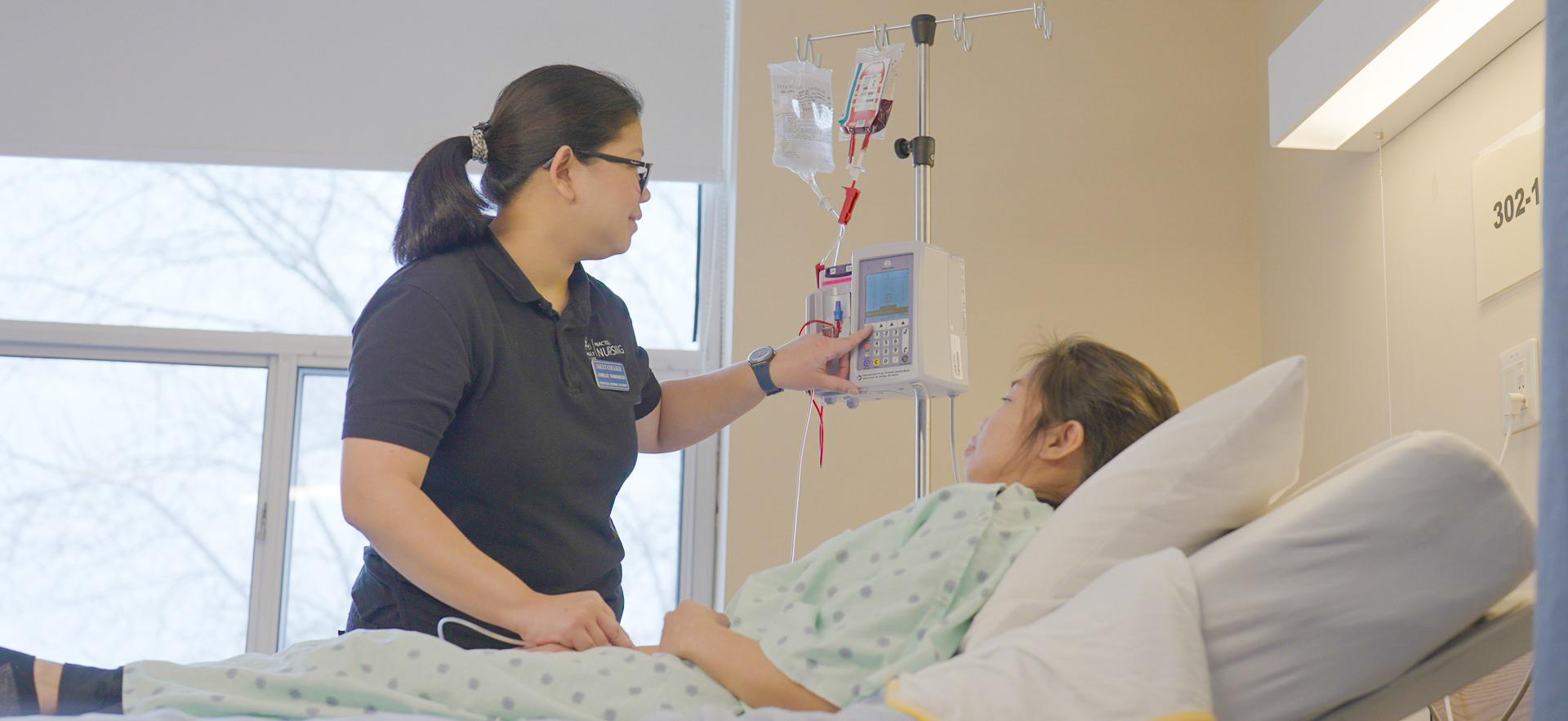 Nursing student adjusting machine for IV of classmate posing as patient