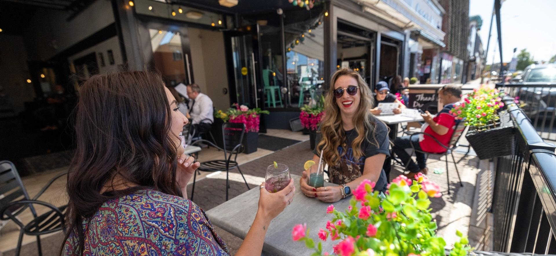 Two women sitting at table talking on downtown patio having a drink