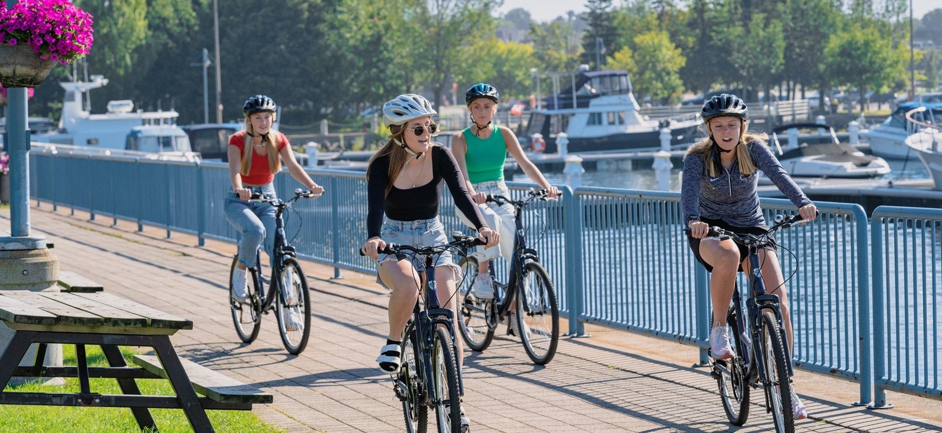 Four women biking on waterfront boardwalk by marina
