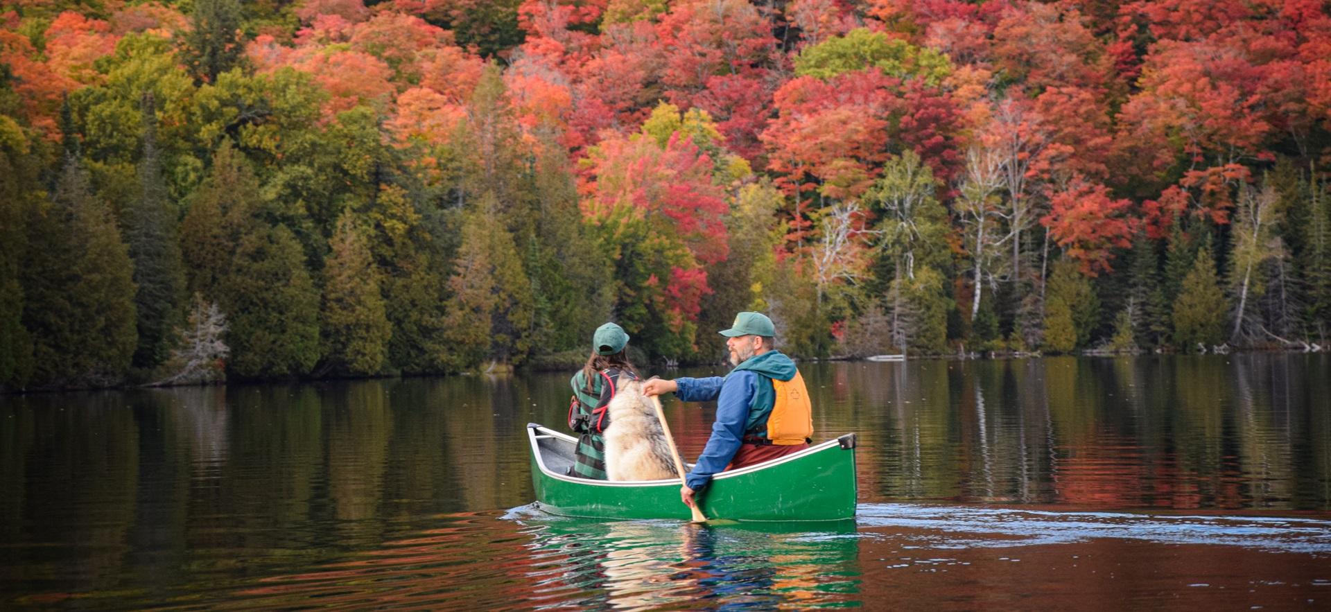 Two people and a dog out in a canoe on the river in the fall