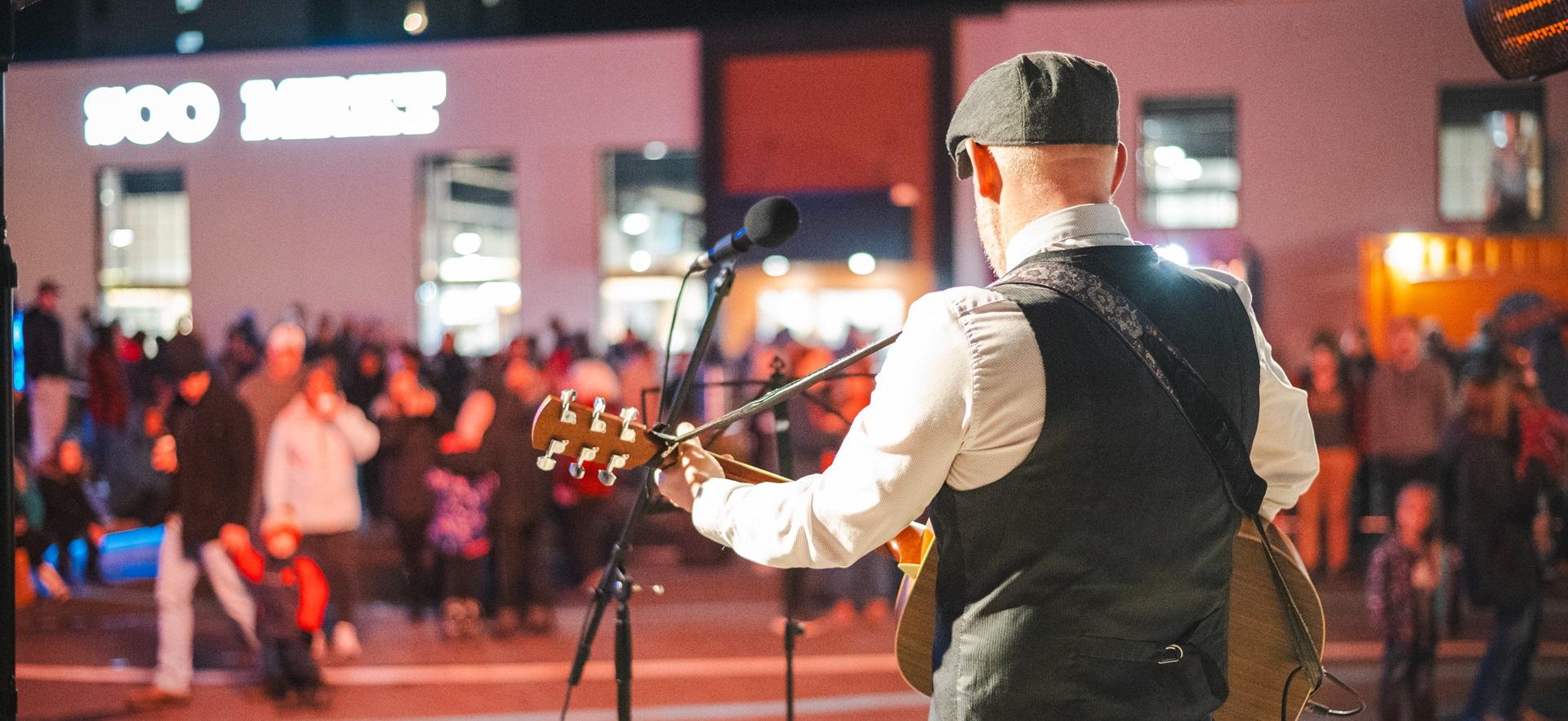 Man playing guitar on stage performing to crowd at Downtown Plaza