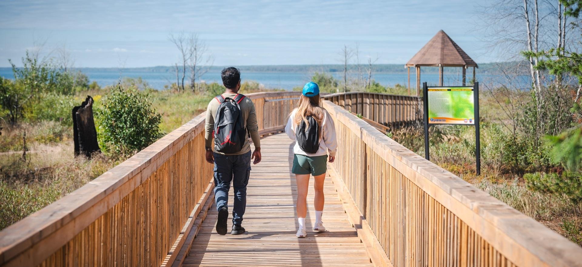Two people walking over a trail bridge at Ojibway