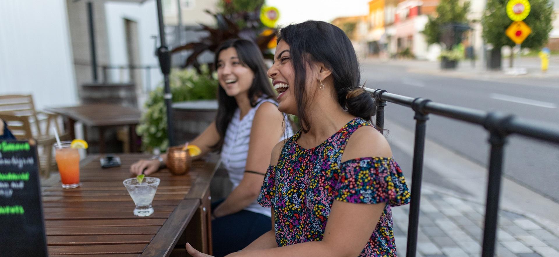 Two women laughing sitting outside on patio at downtown business