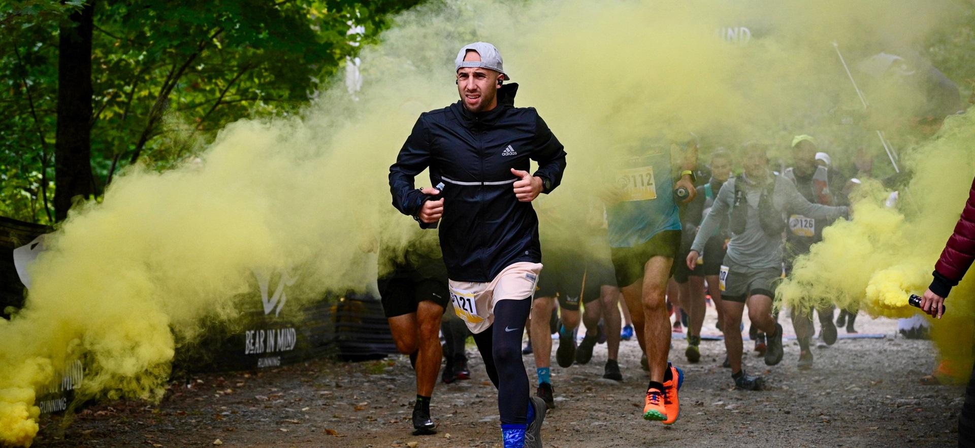 Guy running in race with colourful smoke streaming behind