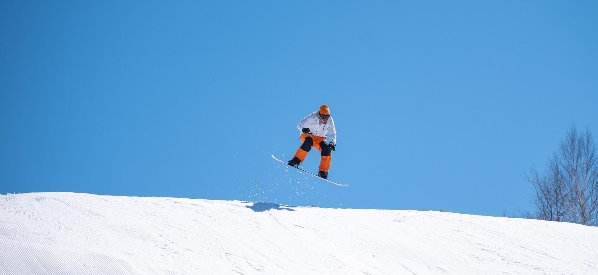 Man snowboarding off a jump on a big hill at Searchmont on a clear sunny day