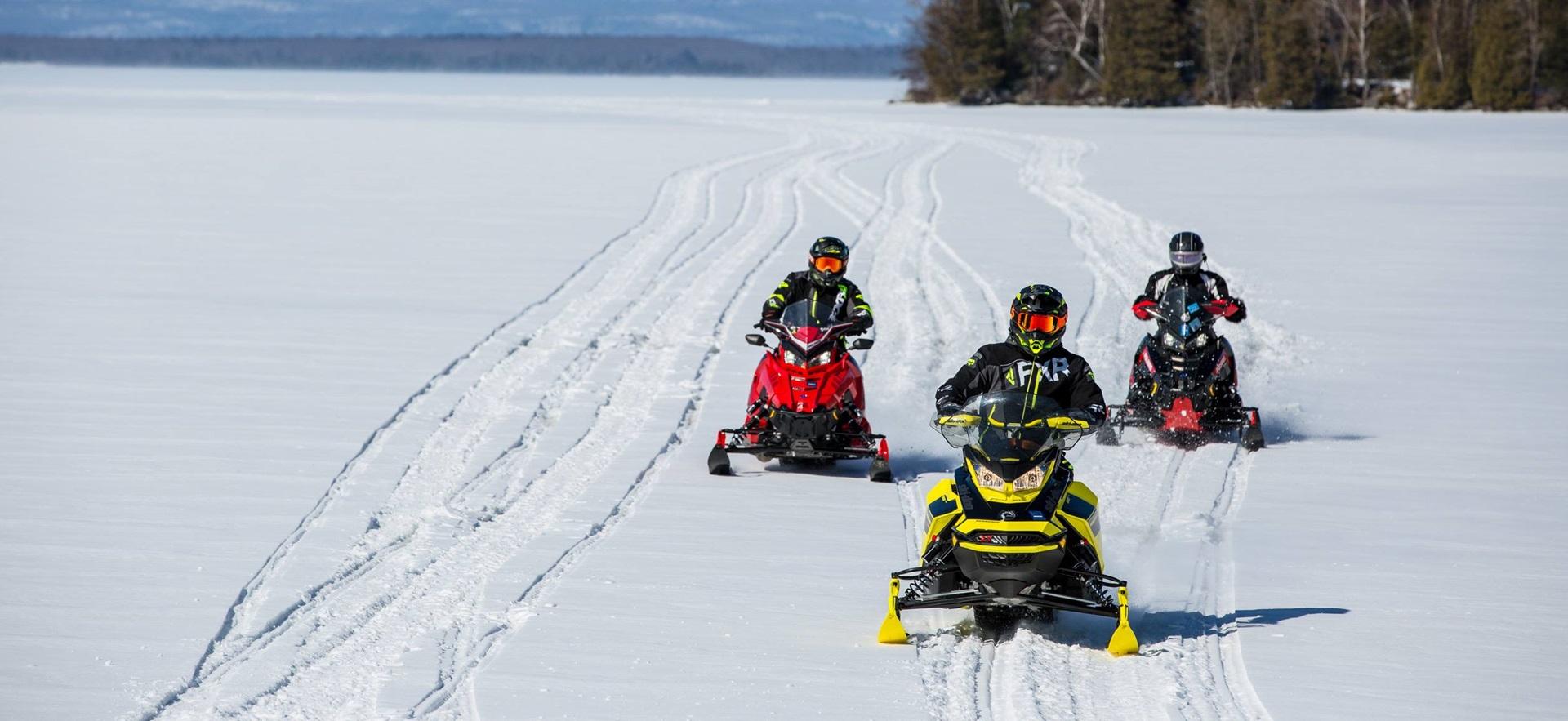 Group of 3 coming down snowy hill on snowmachines