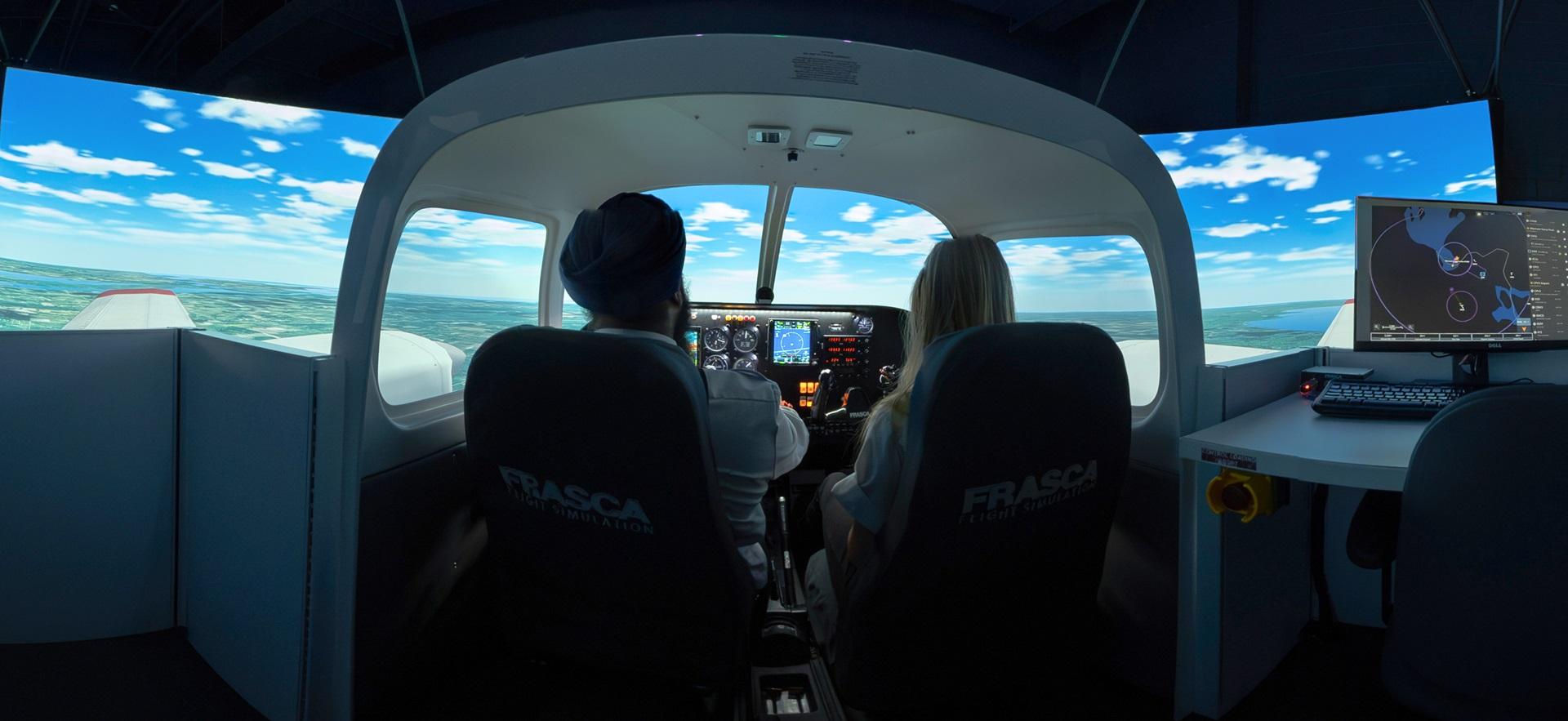 Two aviation students shown from the back sitting in flight simulator