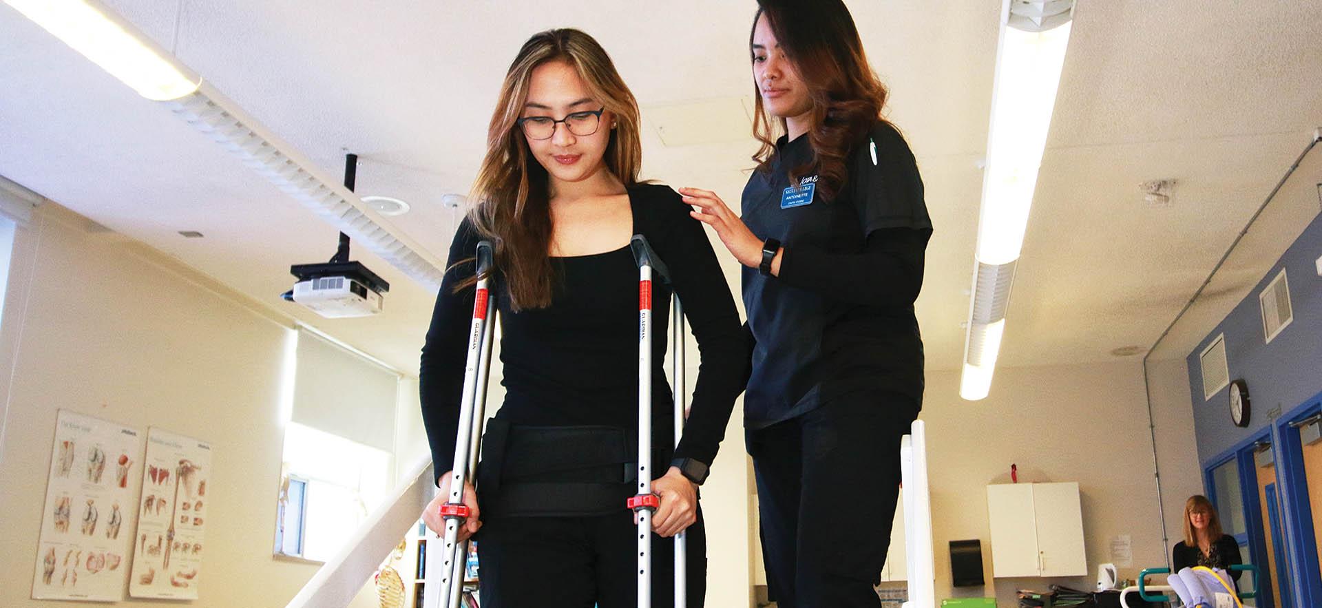 Physiotherapy student assisting another student on crutches
