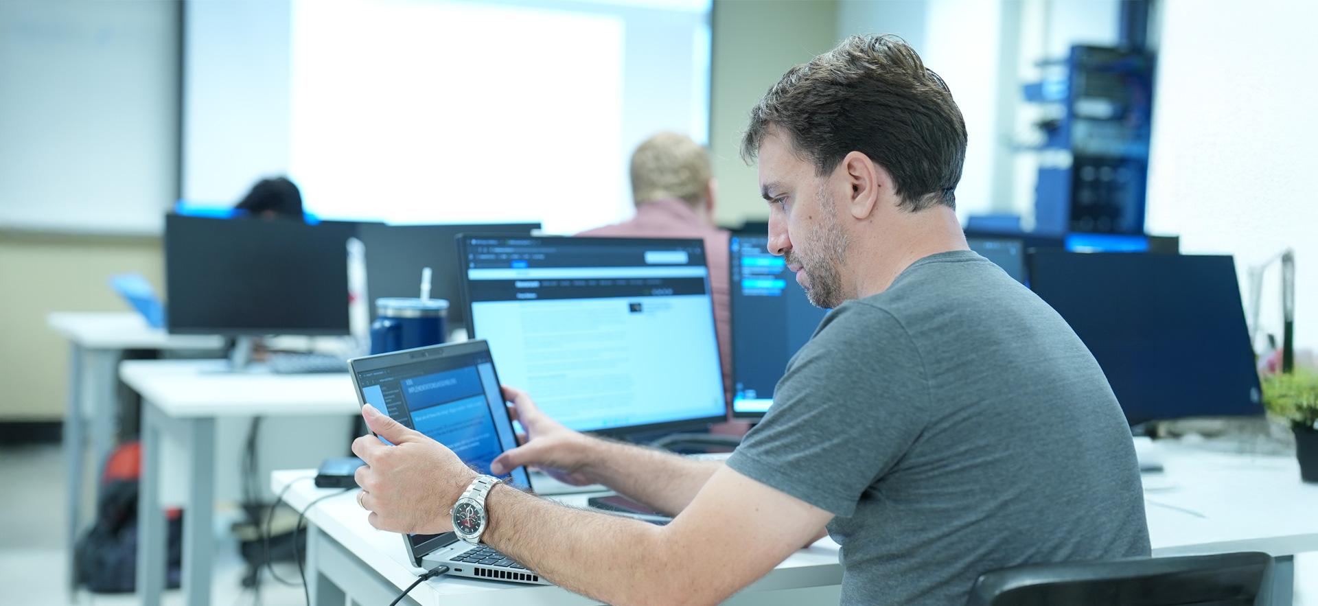IT student sitting at desk in classroom and working on laptop