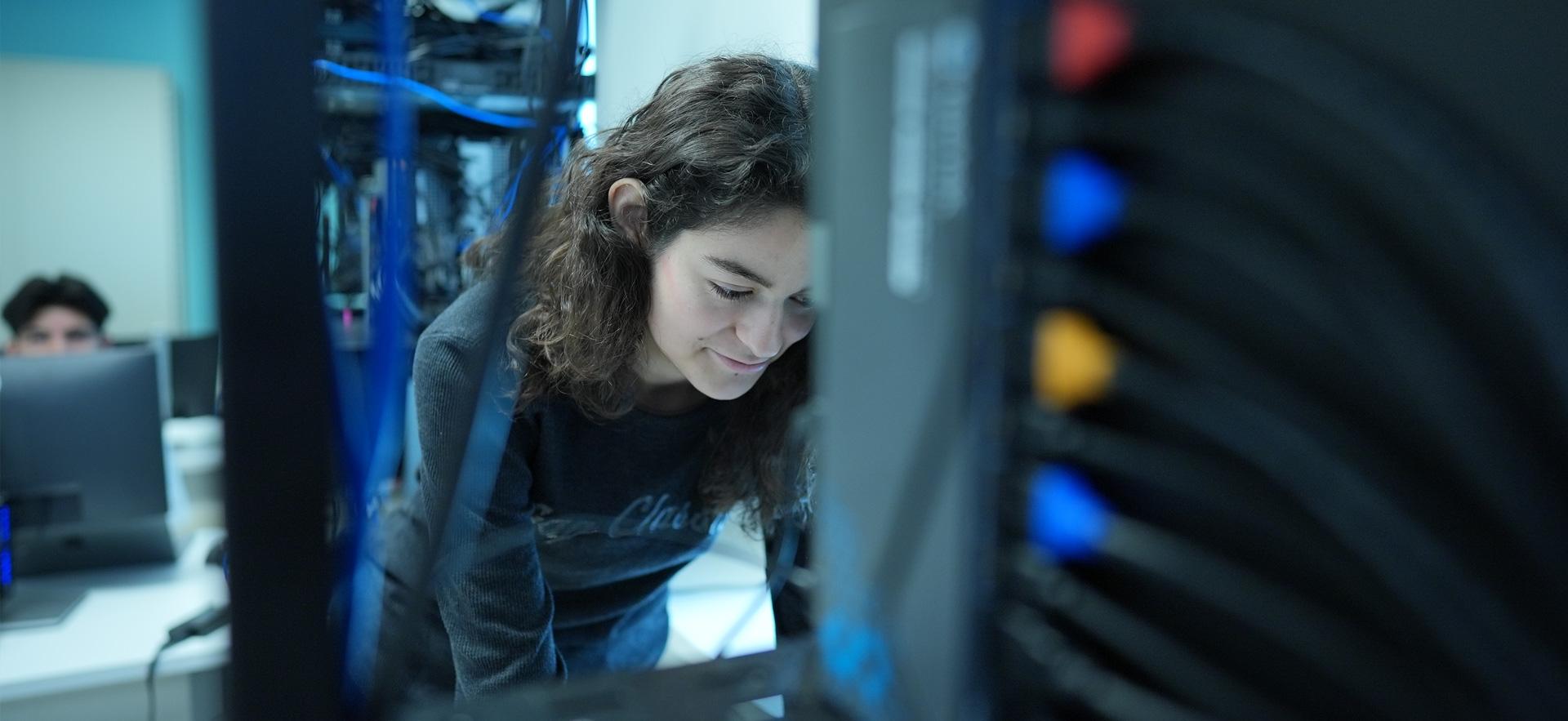 IT student standing at networking stacks leaning over typing on keyboard