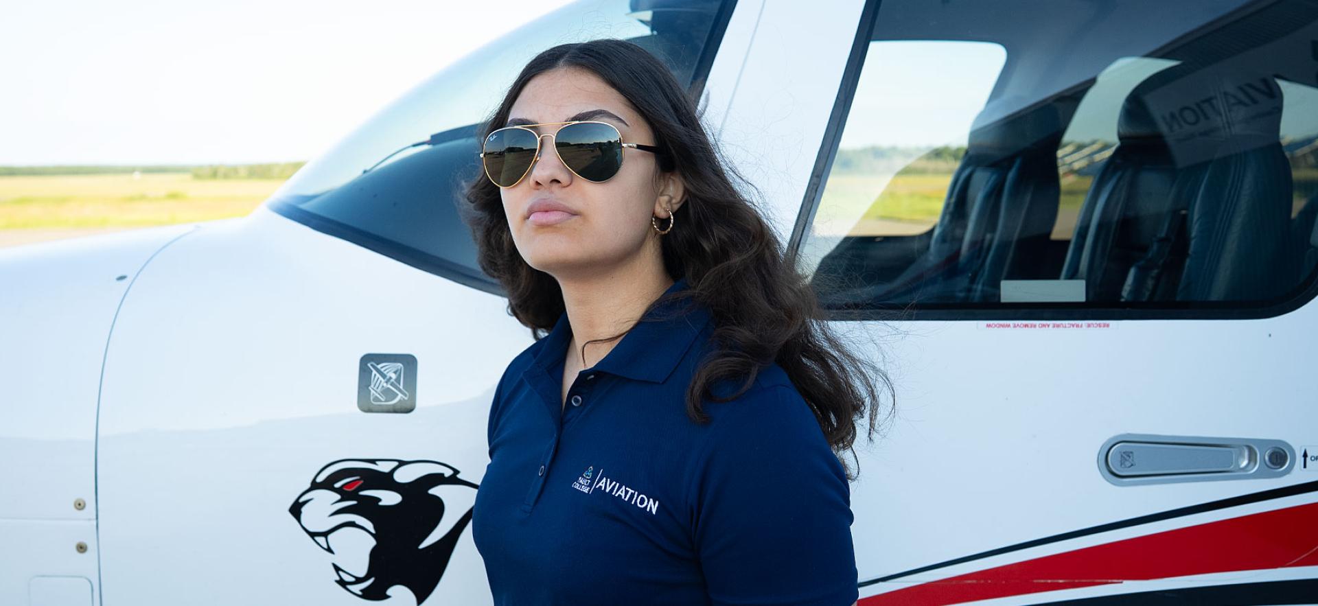 Aviation student with sunglasses on standing in front of plane at Hangar