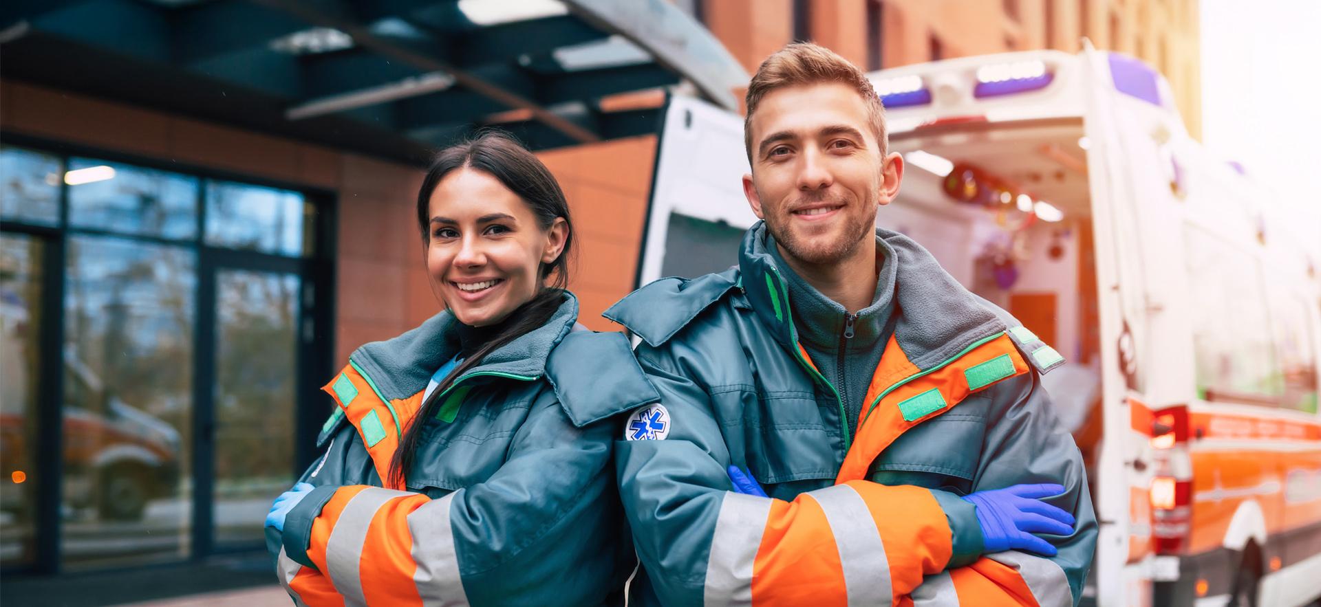 Two paramedics smiling with arms crossed in uniform with ambulance in background