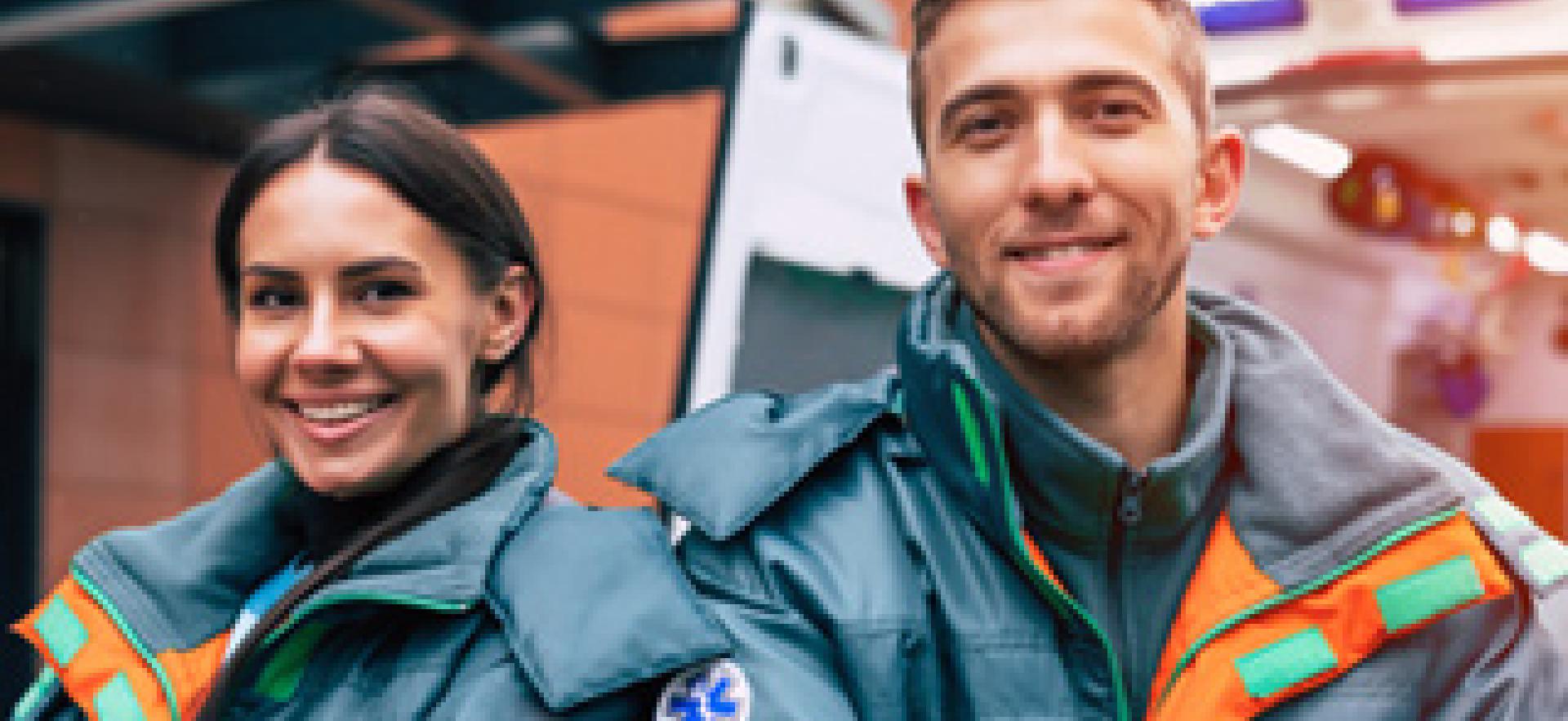 Two paramedics smiling with arms crossed in uniform with ambulance in background