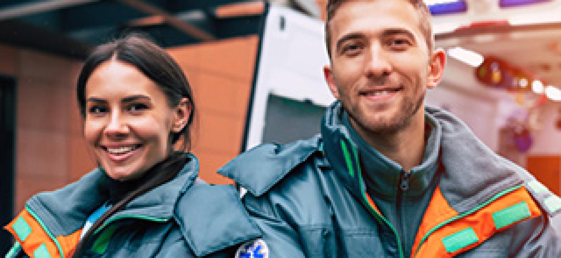 Two paramedics smiling with arms crossed in uniform with ambulance in background