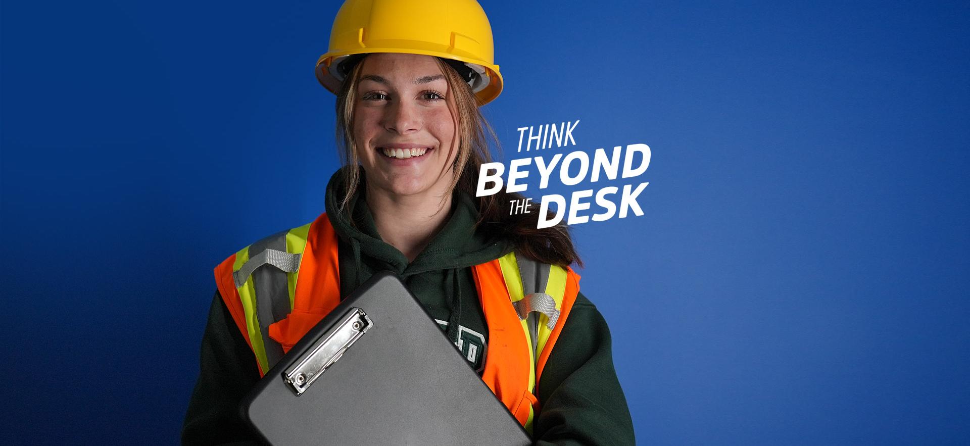 School of Natural Environment student posed for camera with vis vest, hard hat and clipboard