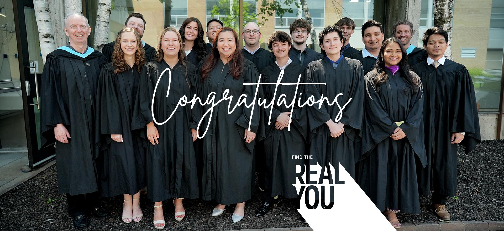 Group of graduating students with faculty in grad gowns posed together outdoors
