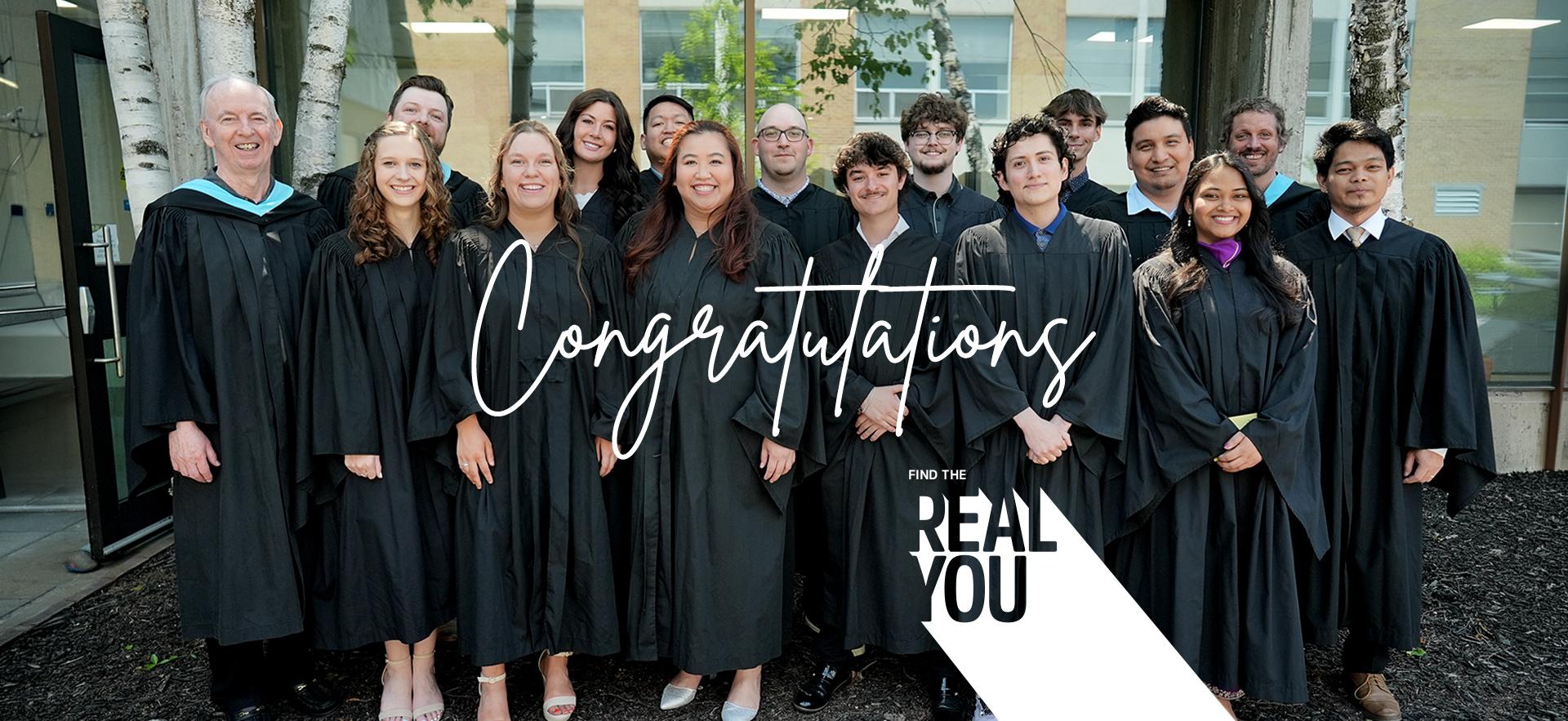 Group of graduating students with faculty in grad gowns posed together outdoors